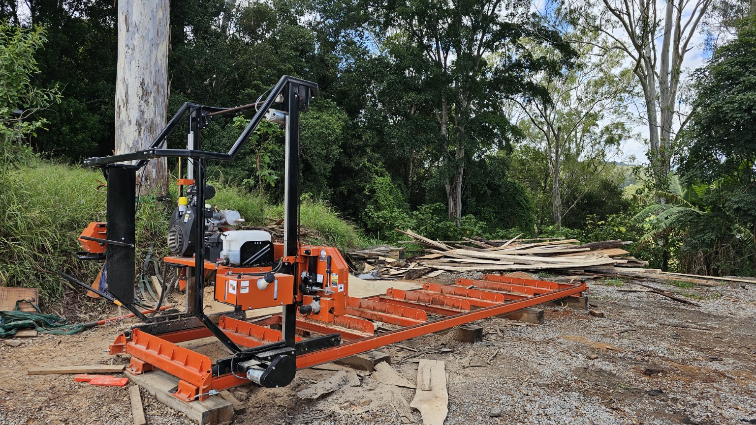 Orange portable sawmill in an outdoor timber processing yard